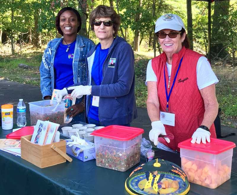 3 female volunteers at a table outdoors offering fresh produce