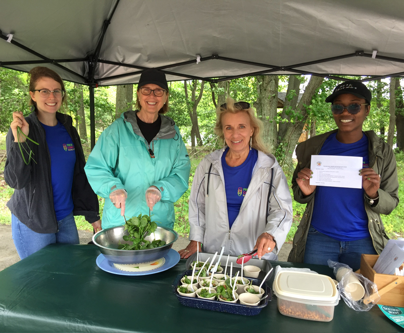 4 female volunteers at a table outdoors offering fresh produce spinach salads