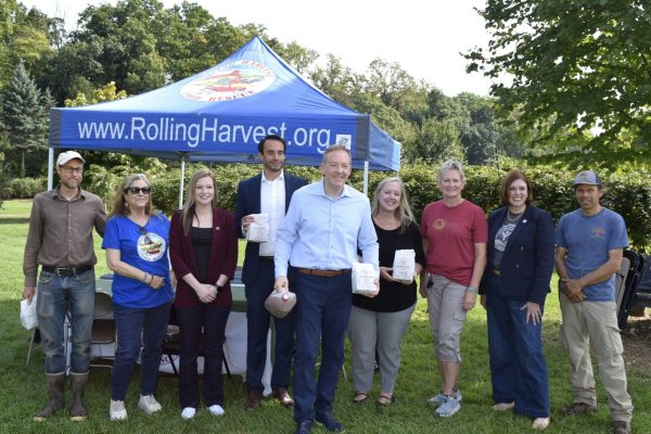 Group photo of EPA Administrator Lee Zeldin and community members at Solebury Orchards, standing beneath a Rolling Harvest Food Rescue tent and holding bags of food.