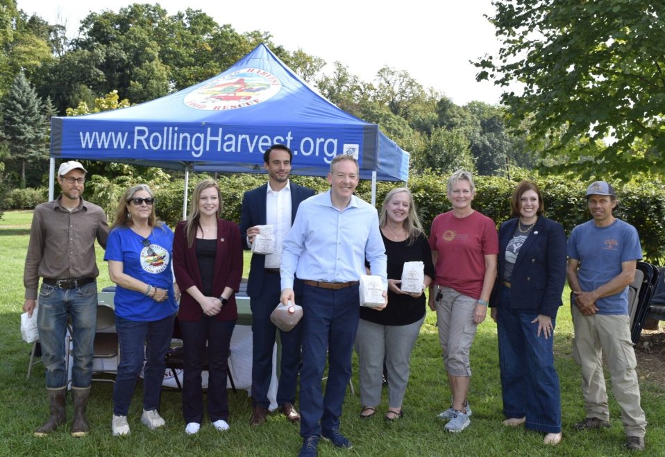 Group photo of EPA Administrator Lee Zeldin and community members at Solebury Orchards, standing beneath a Rolling Harvest Food Rescue tent and holding bags of food.